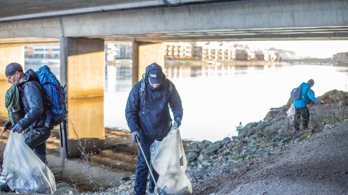 Tre mennesker som plukker søppel med plukkeklyper under en bro.