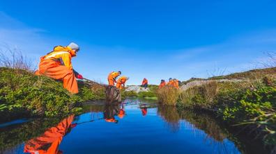Person in orange workwear clearing a pond.