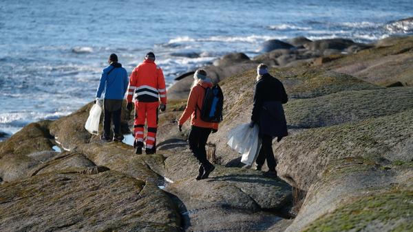 Four persons walks by the ocean carrying clean-up bags.