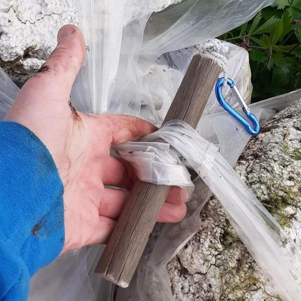 Hand holding an old broom handle. Litter bags are attached to the shaft.