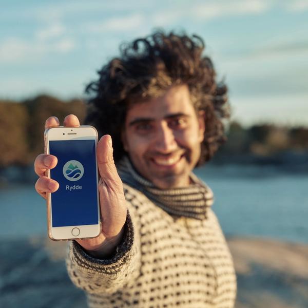 En person holder opp en mobil som viser Rydde sin logo på skjermen.