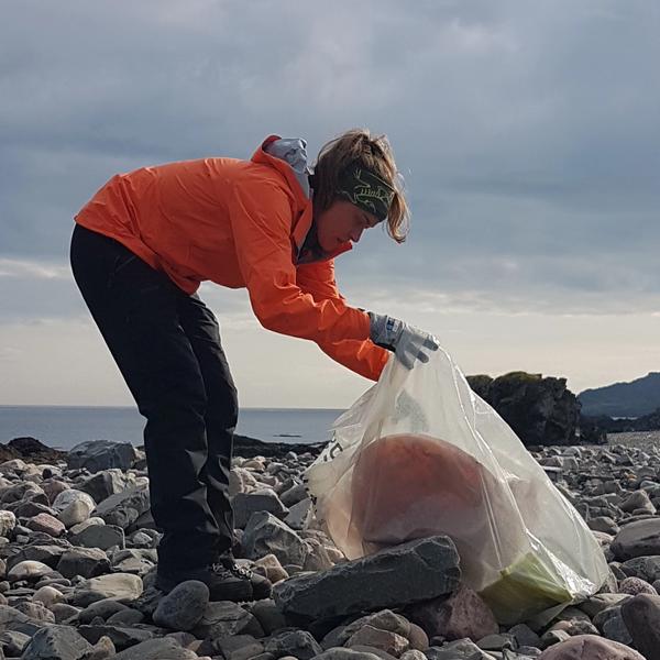 Person wearing orange clothing is cleaning litter from a beach.