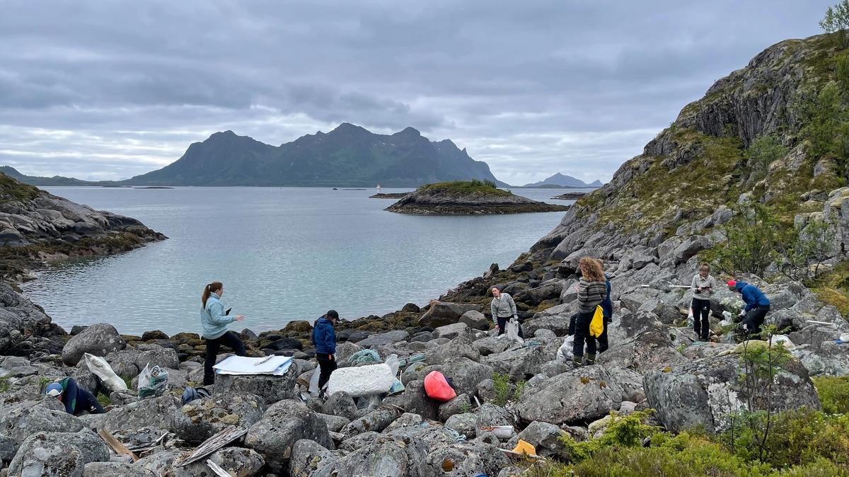 People clearing litter in a cove. Sea and mountains in the background.