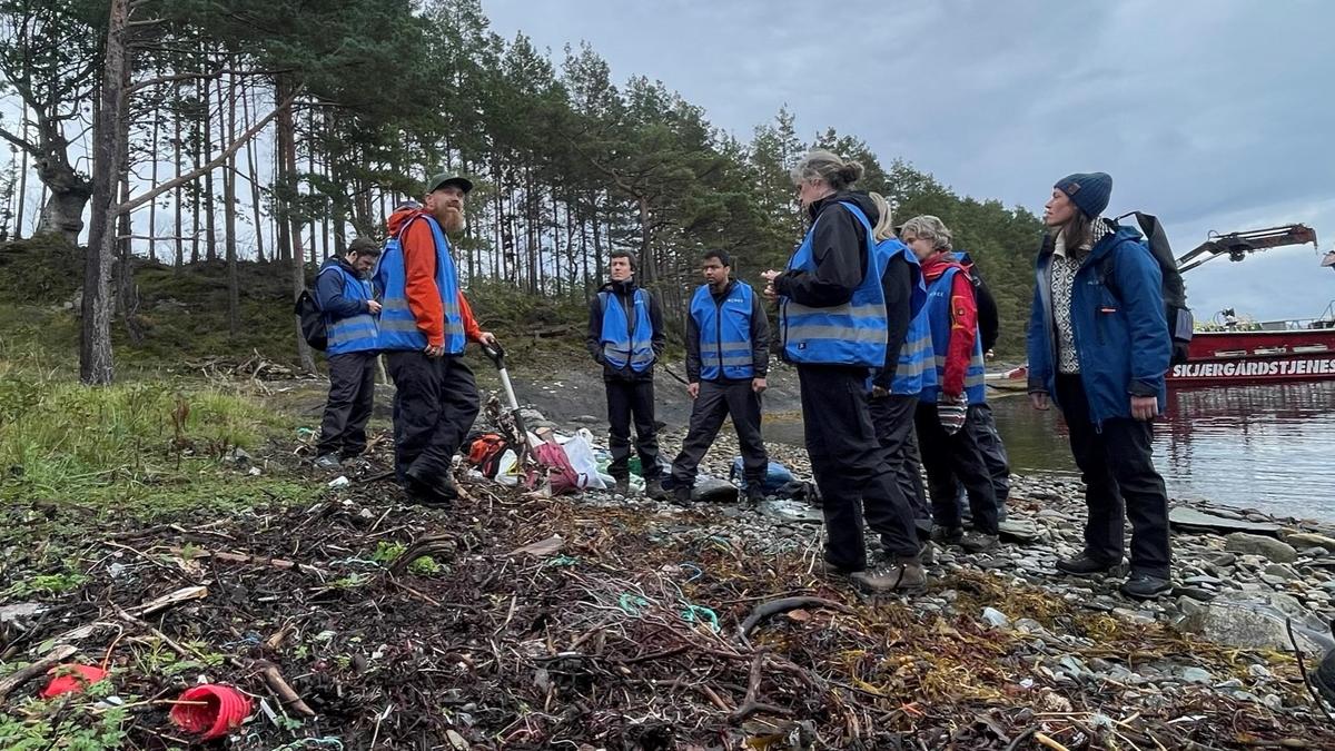  Group of cleaners stand on a beach with rubbish and receive information.