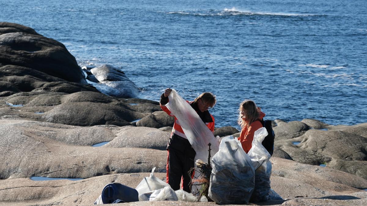 To personer på svaberg ved havet, som organiserer søppelsekker.