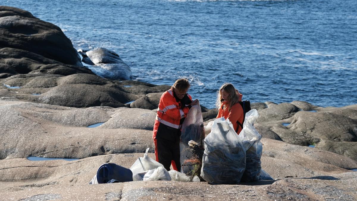 Hav og kyst. Plastforsøpling i forgrunnen og mennesker som sitter ved en båt i bakgrunnen.