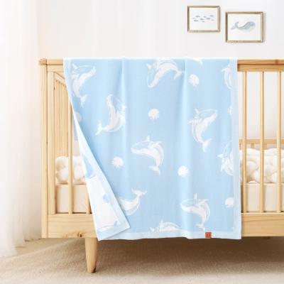 Baby crib with a blue jacquard knit baby blanket featuring white whale patterns in a nursery setting.