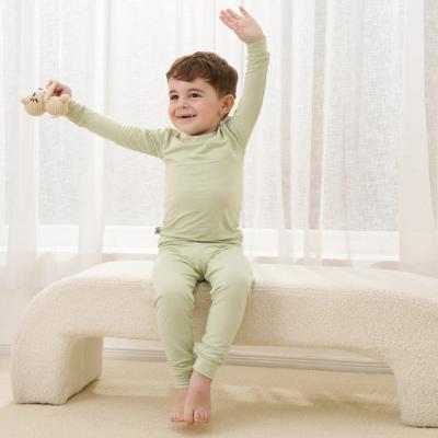Child wearing a green two-piece pajamas sitting on a white couch with white curtains in the background
