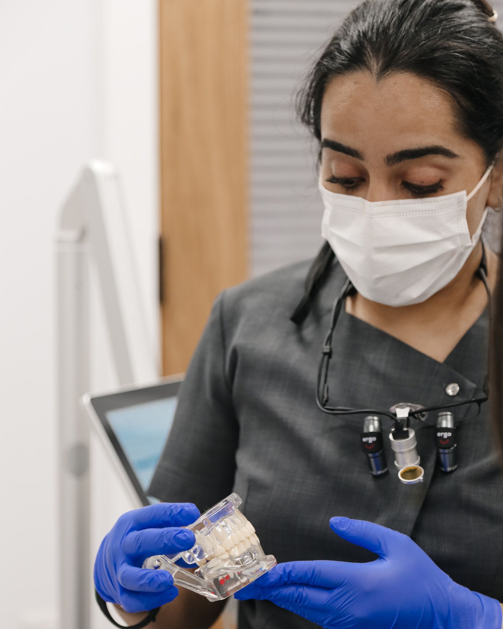 Dental clinician in scrubs and loupes examining a dental jaw model