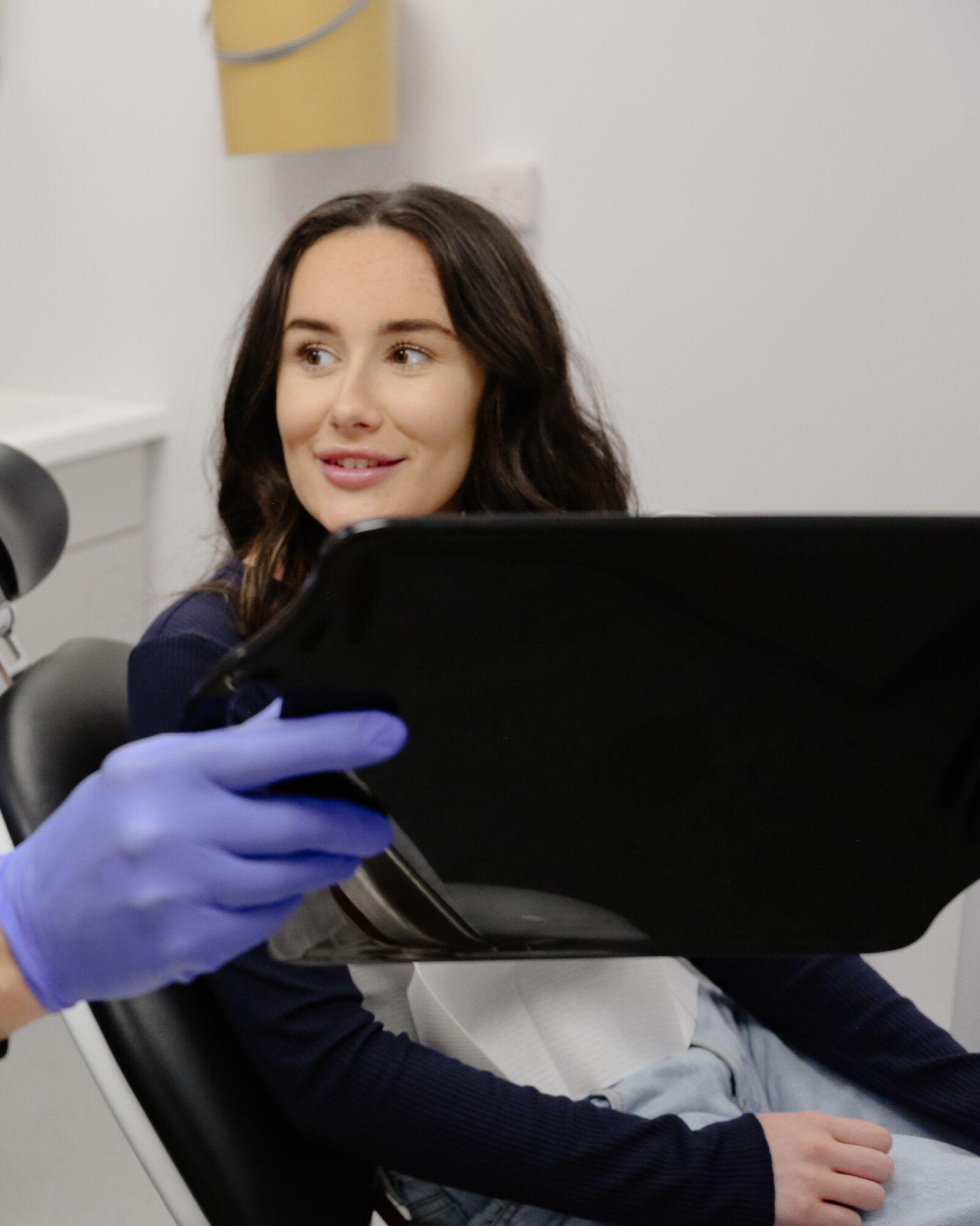 Patient in a dental chair smiling as a clinician shows her treatment information on a tablet