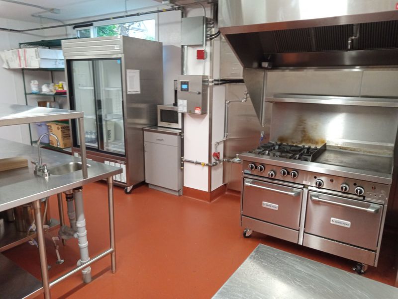 The kitchen's gas range and griddle beside the stainless prep tables