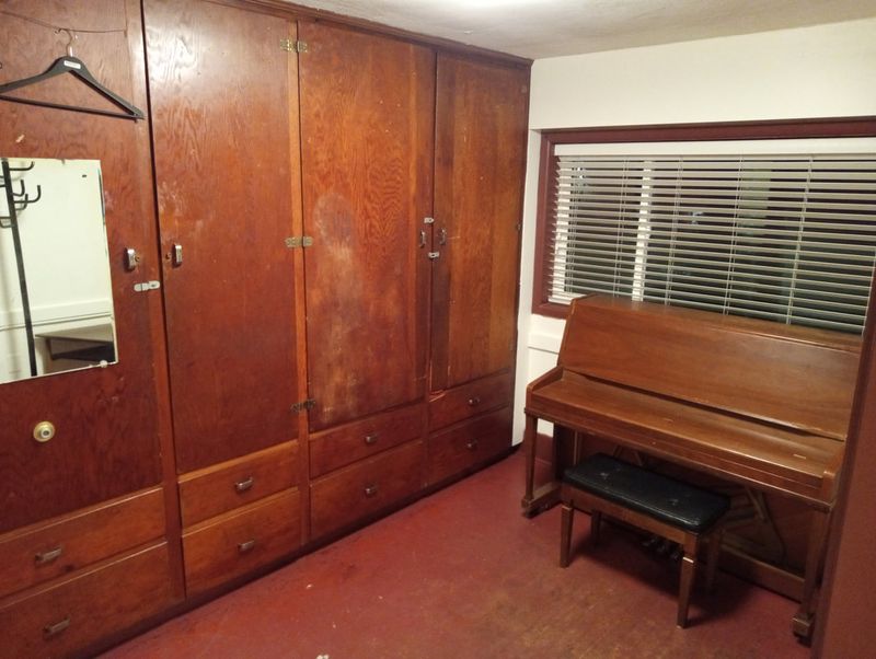 A dressing room with a wooden wardrobe, mirror and upright piano