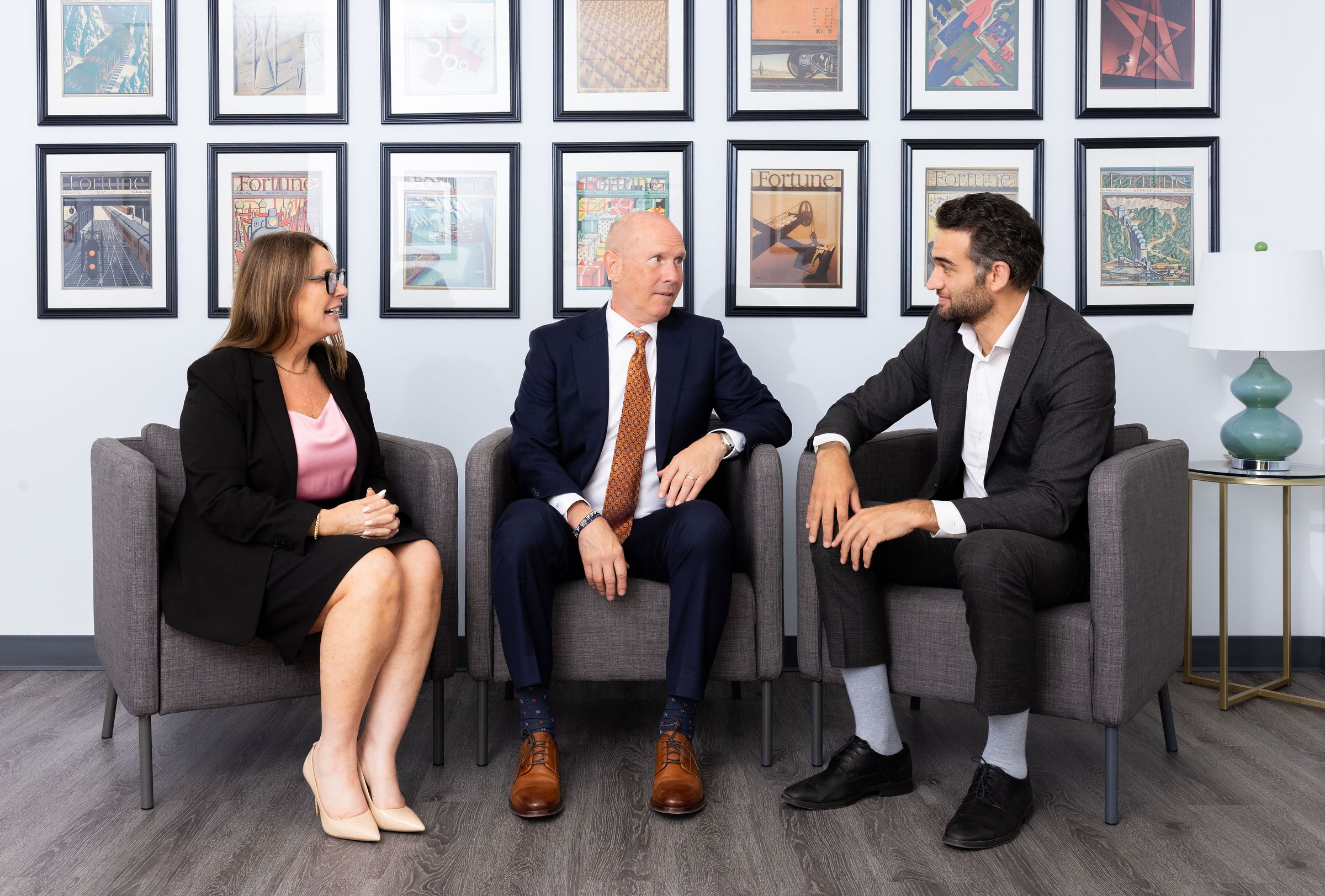 Three Omnigence private equity colleagues in conversation, seated beneath a wall of framed vintage Fortune magazine covers