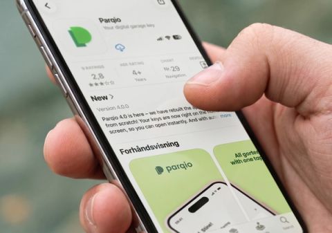 A hand holds a smartphone displaying the Parqio app listing on the Norwegian App Store, showing version 4.0.0 details and preview screenshots.