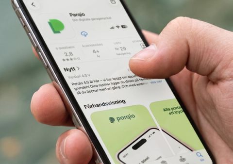 En hand håller en smartphone som visar Parqio-appens listning i norska App Store med version 4.0.0-detaljer och förhandsvisningsbilder.