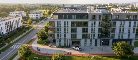 Aerial view of a modern multi-storey residential building with balconies, a curved red cycle path, pedestrians, cyclists, and a white SUV parked at the entrance on a sunny day.