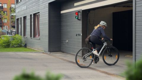 A cyclist wearing a helmet rides into an open garage entrance of a gray building with a red and green traffic light above the doorway.