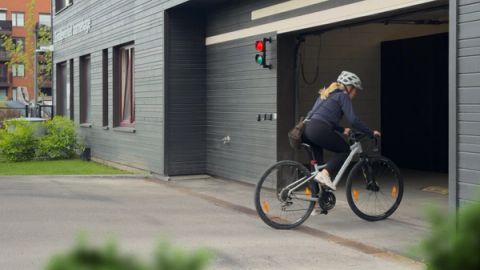 A cyclist wearing a helmet rides into an open garage entrance of a gray building with a red and green traffic light above the doorway.