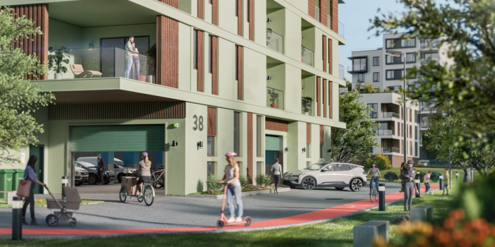 People walk, cycle, and ride scooters along a red path in front of a modern green apartment building with balconies and parked cars.