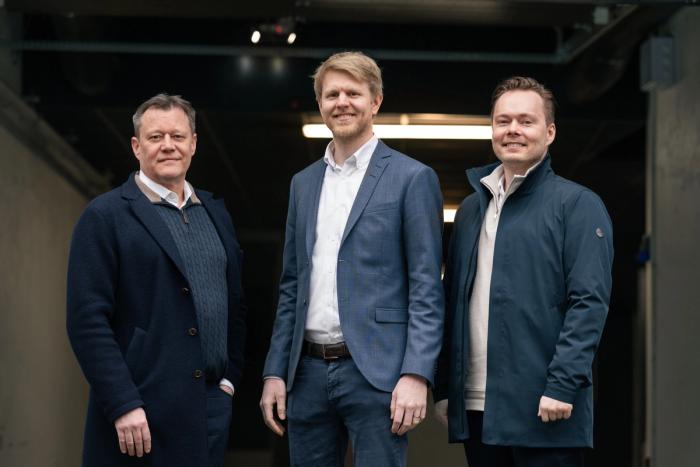 Three men in smart casual business attire stand side by side indoors, facing the camera and smiling slightly.