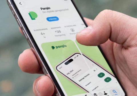 En hand håller en smartphone som visar Parqio-appens listning i norska App Store med version 4.0.0-detaljer och förhandsvisningsbilder.