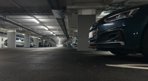 Dimly lit underground parking garage with rows of parked cars on both sides and concrete pillars running down the center.
