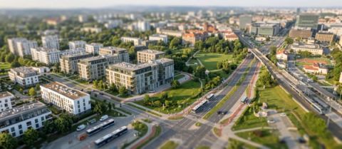 Aerial tilt-shift photograph of a modern residential neighbourhood with multi-storey apartment blocks, green parkland, and a wide multi-lane urban road with buses and cars.
