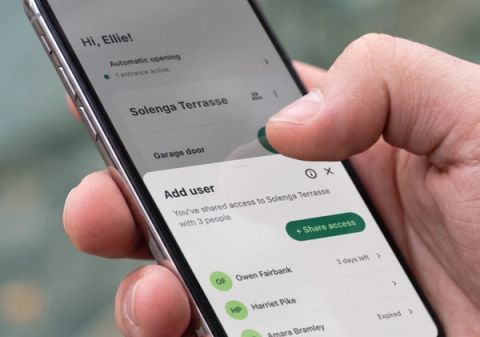 Close-up of a hand holding a phone with the Parqio app open on “Add user” – access to Solenga Terrasse is shared with three people.