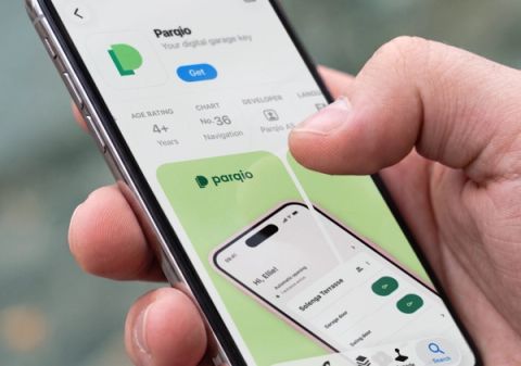 A hand holds a smartphone displaying the Parqio app listing on the Norwegian App Store, showing version 4.0.0 details and preview screenshots.