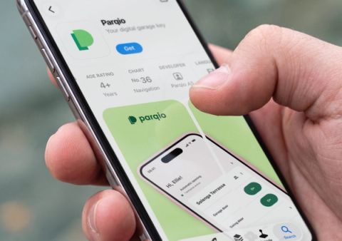 A hand holds a smartphone displaying the Parqio app listing on the Norwegian App Store, showing version 4.0.0 details and preview screenshots.