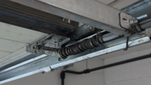 Close-up of a metal garage door track and torsion spring mechanism mounted to the ceiling.