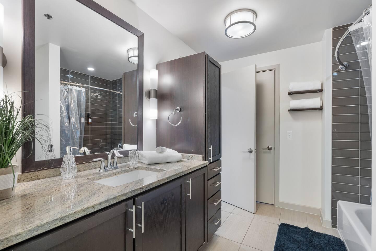 Bathroom with bathtub, toilet , vanity , big mirror, fresh towels , consumables include shampoo, conditioner, body wash, hair dryer.