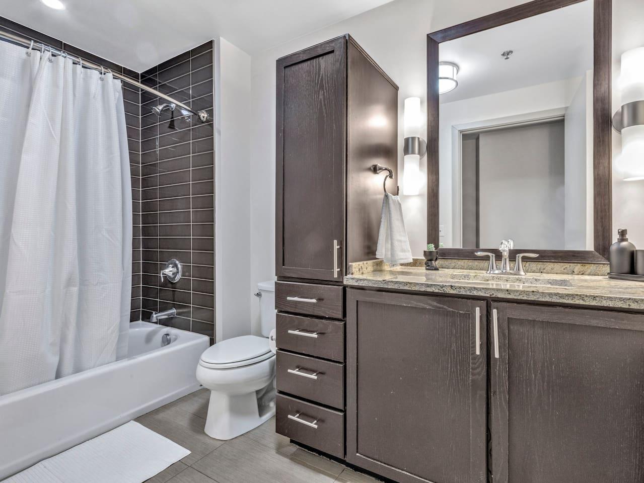 Bathroom with bathtub, toilet , vanity , big mirror, fresh towels , consumables include shampoo, conditioner, body wash, hair dryer.
