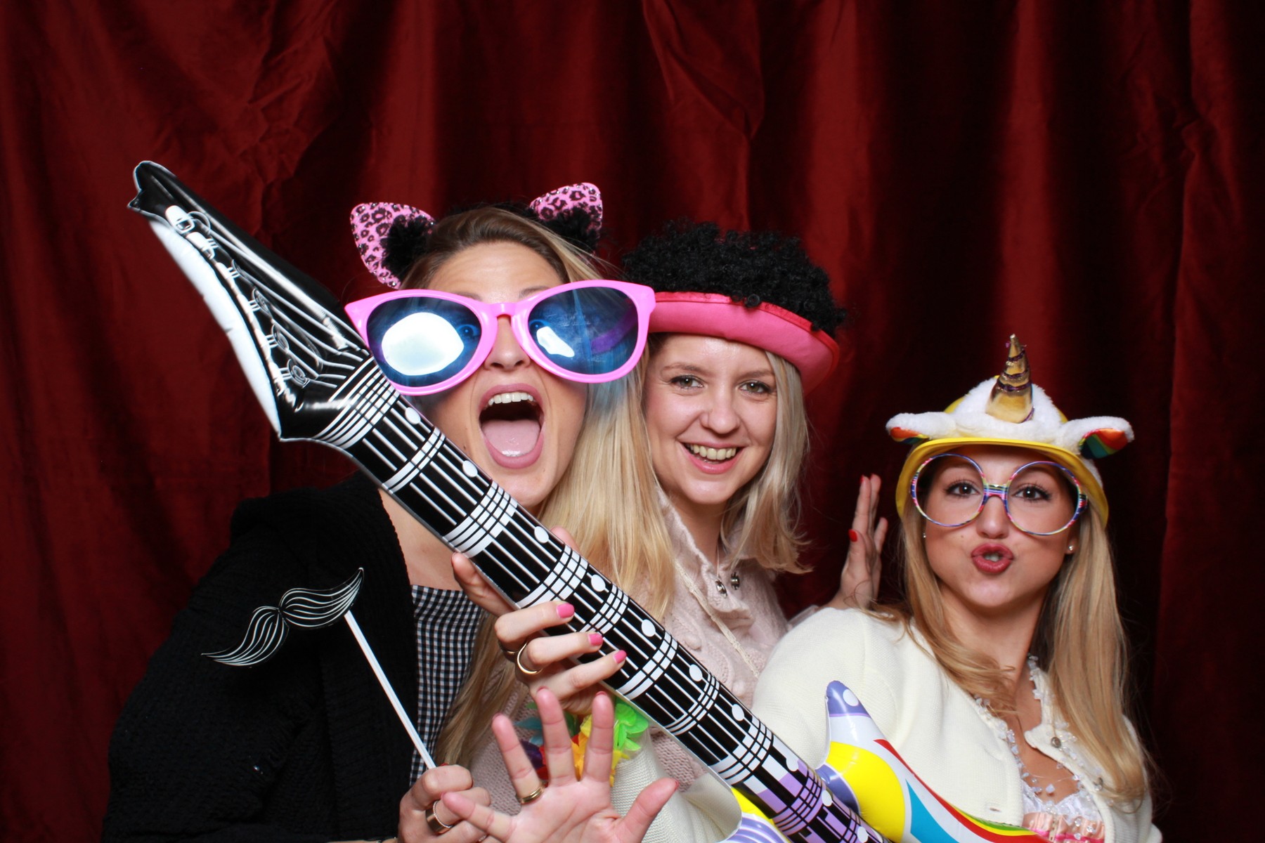 Vier Gäste feiern mit Hüten, Brillen und Luftgitarre vor der Fotobox