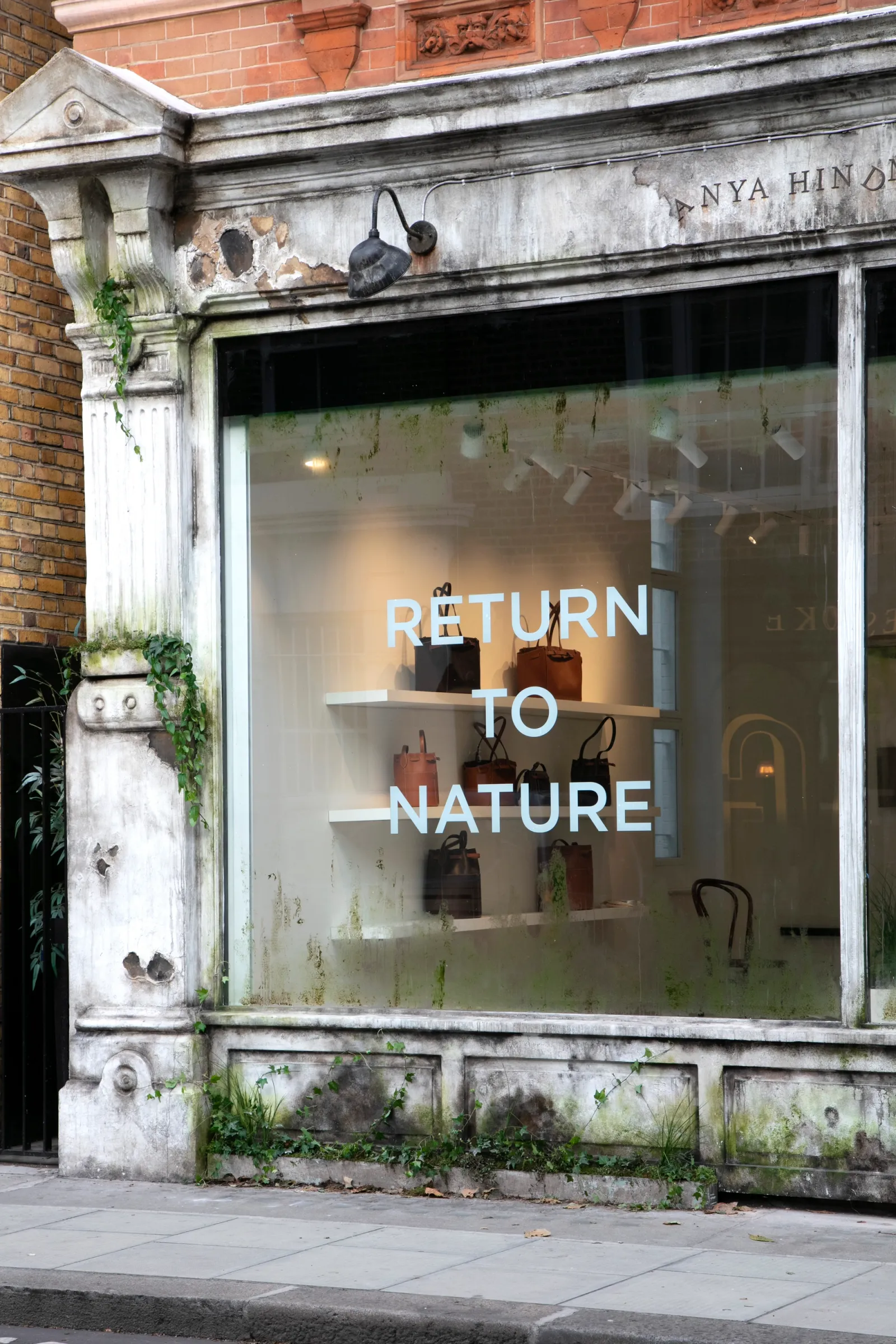 Weathered Anya Hindmarch shopfront with ivy growing from cracks and 'Return to Nature' lettering on the window