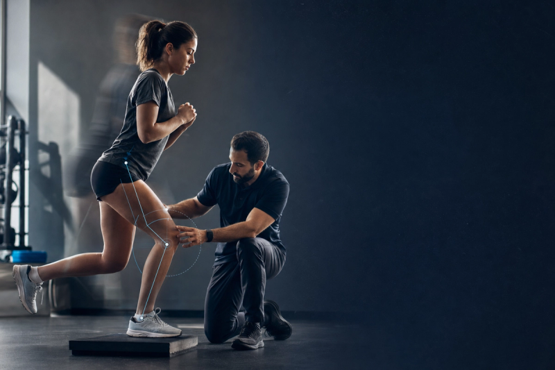 Physical therapist checking an athlete's knee during a supervised single-leg exercise in ACL prehab, with subtle joint-angle analysis cues