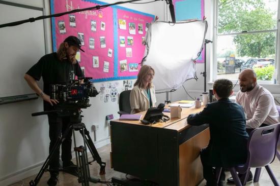 cameraman and actors at a desk in a school having a parents meeting with the teacher