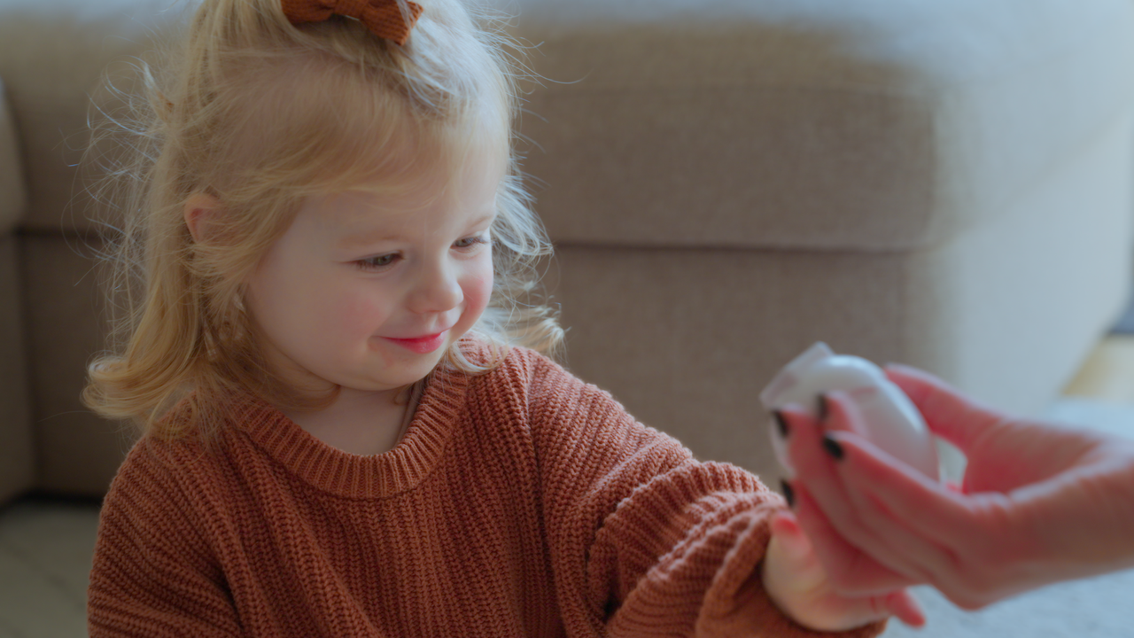 little girl playing with toy handed by parent