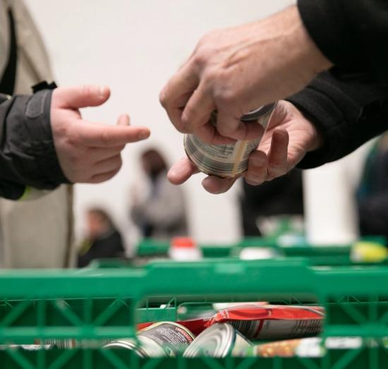 person at foodbank giving a tin to someone