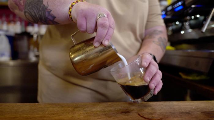 barista pouring milk into coffee