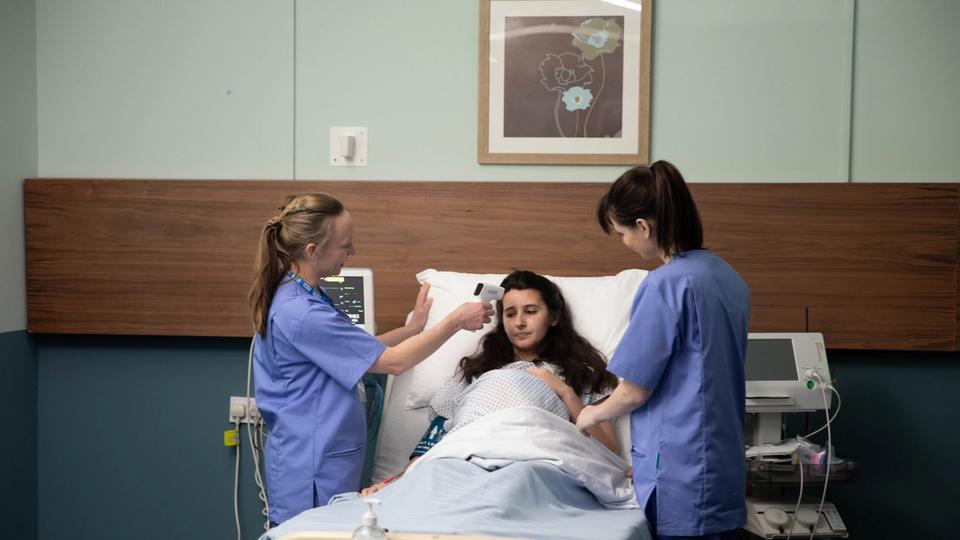 pregnant woman in hospital bed with 2 midwives taking temperature