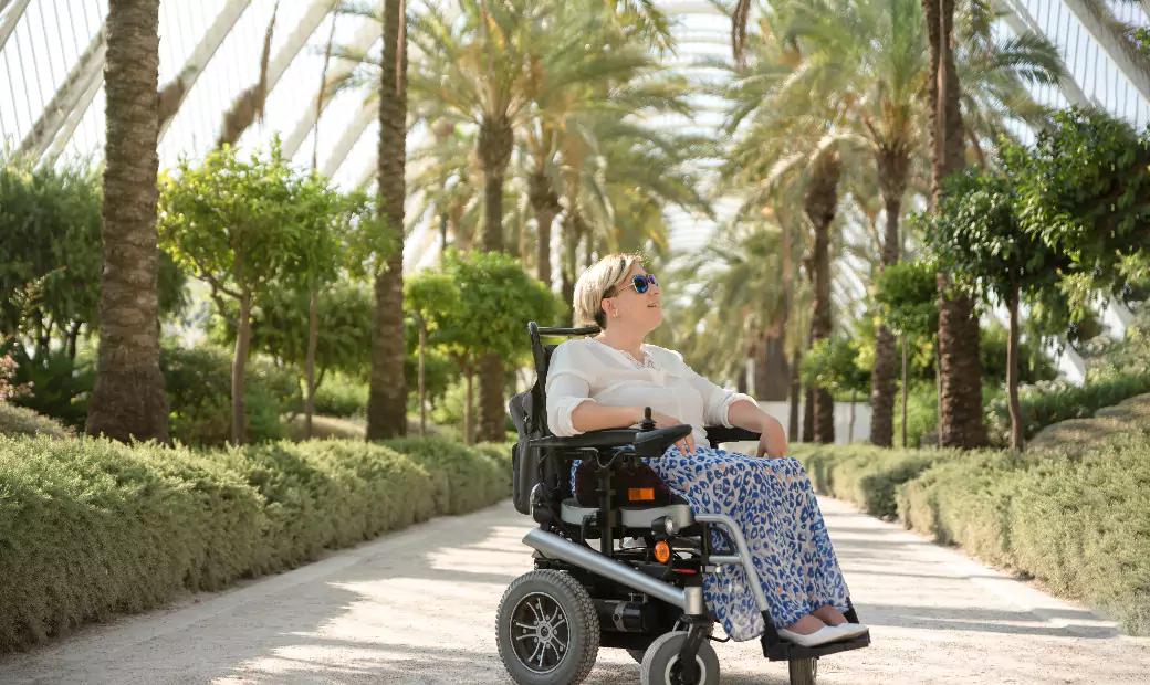 a-smiling-woman-sitting-in-the-electric-wheelchair-with-disability-enjoys-a-sunny-day-in-the-garden-of-the-city-park