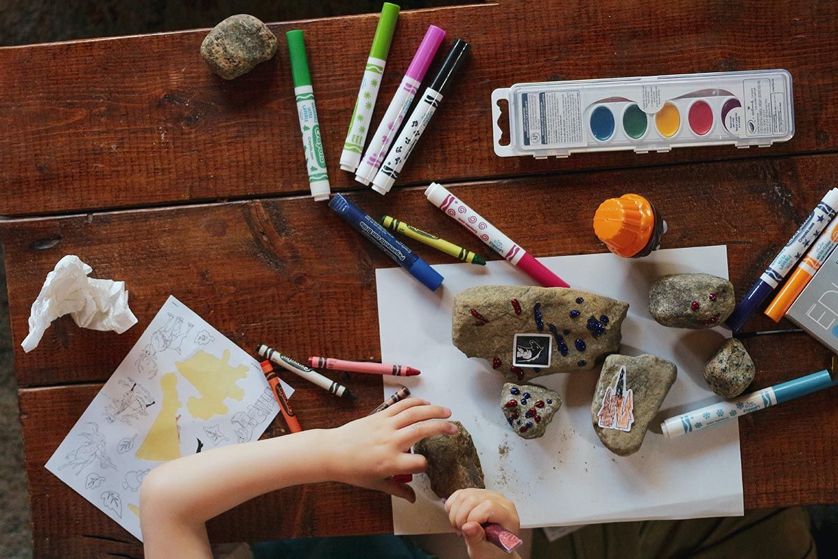 Photo of a table with a lot of crafts and a kid's hands creating something