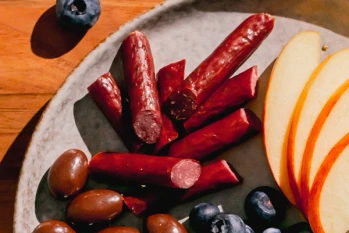 A charcuterie plate filled with blueberries, sliced apples, chocolate covered almonds and Maui Nui venison sticks.