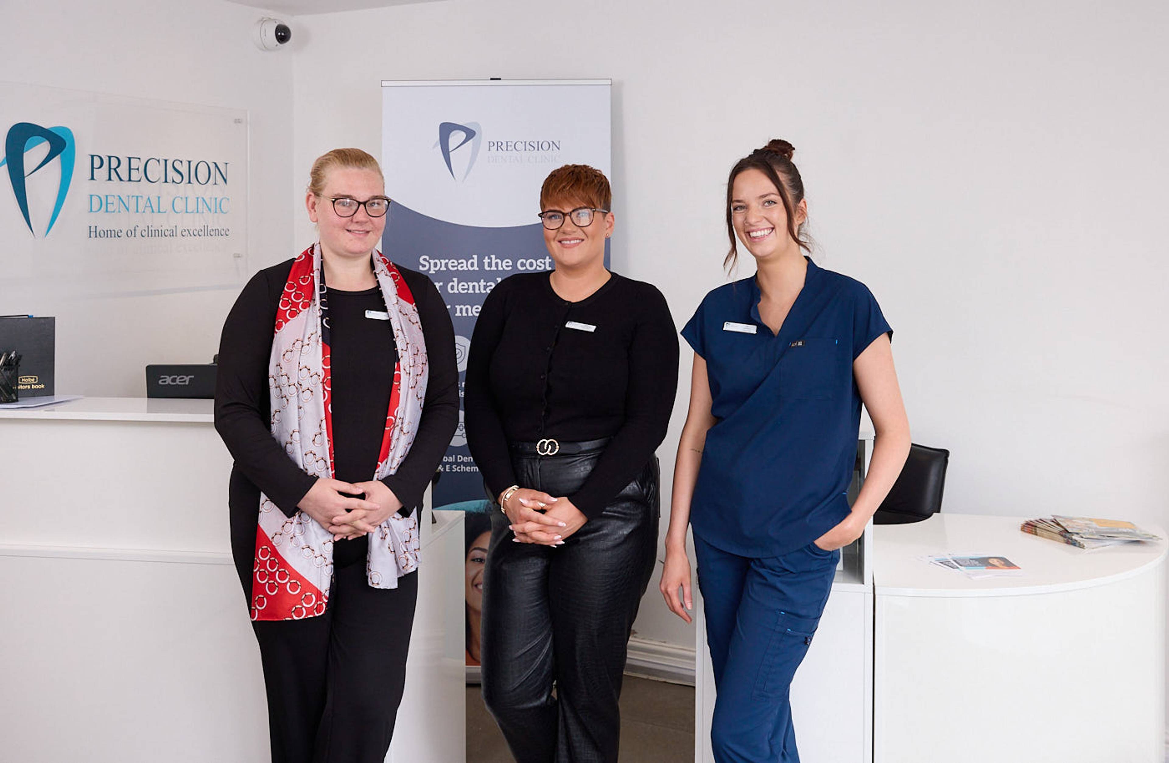 three female dental professionals standing in front of customer help desk in patient waiting area smiling