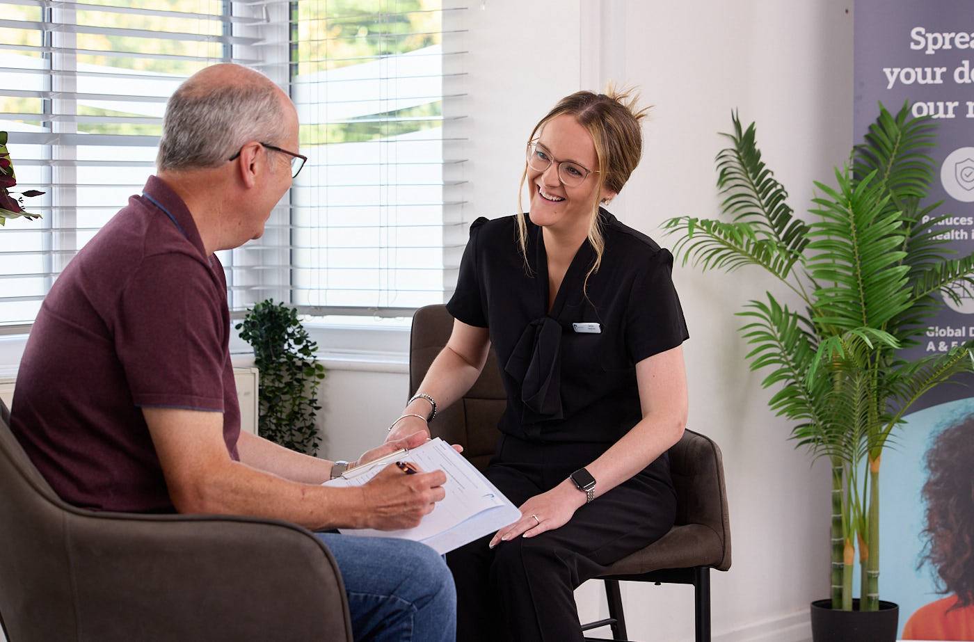 Female receptionist sat with patient next to large sunny window discussing patient finance information