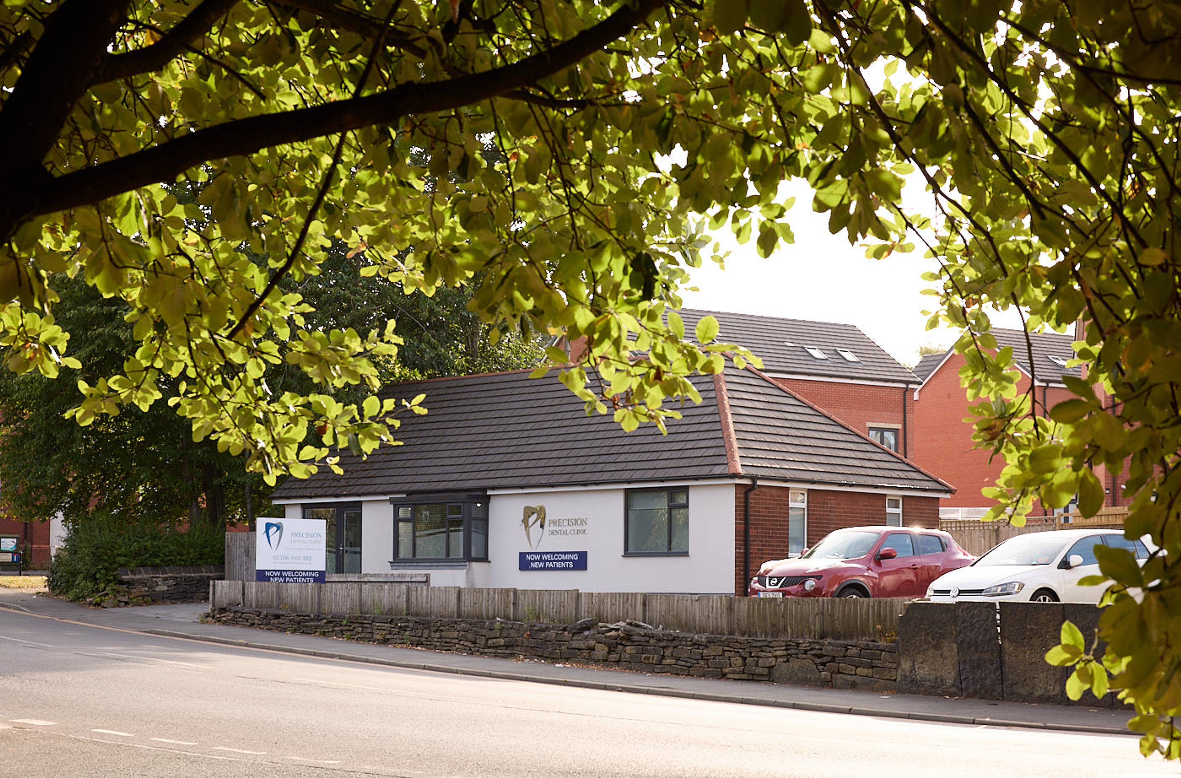 View of outside Precision Dental Clinic Oldham amongst green leafy trees