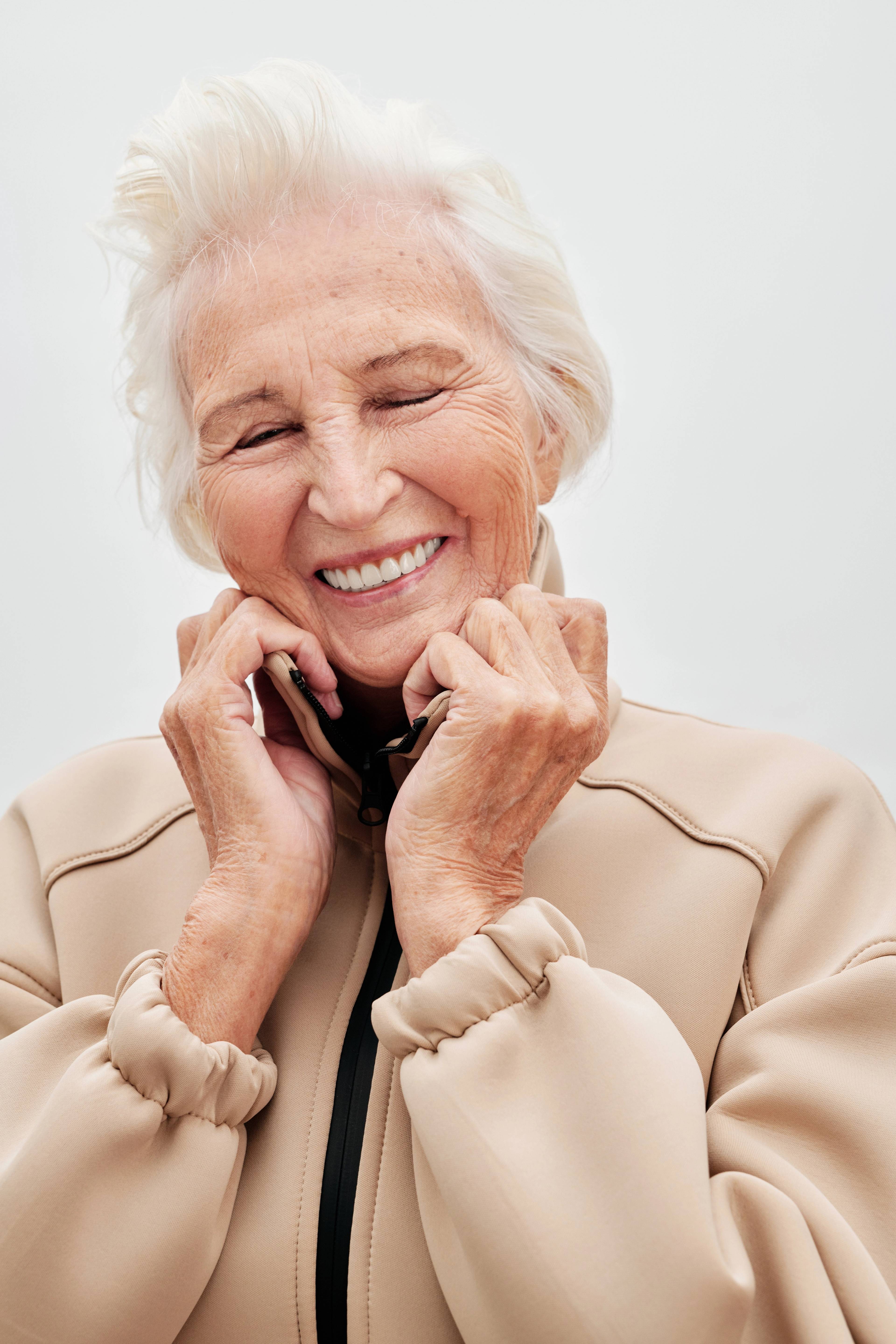 female patient with white hair and pink jacket smiling showing teeth in light sunny environment