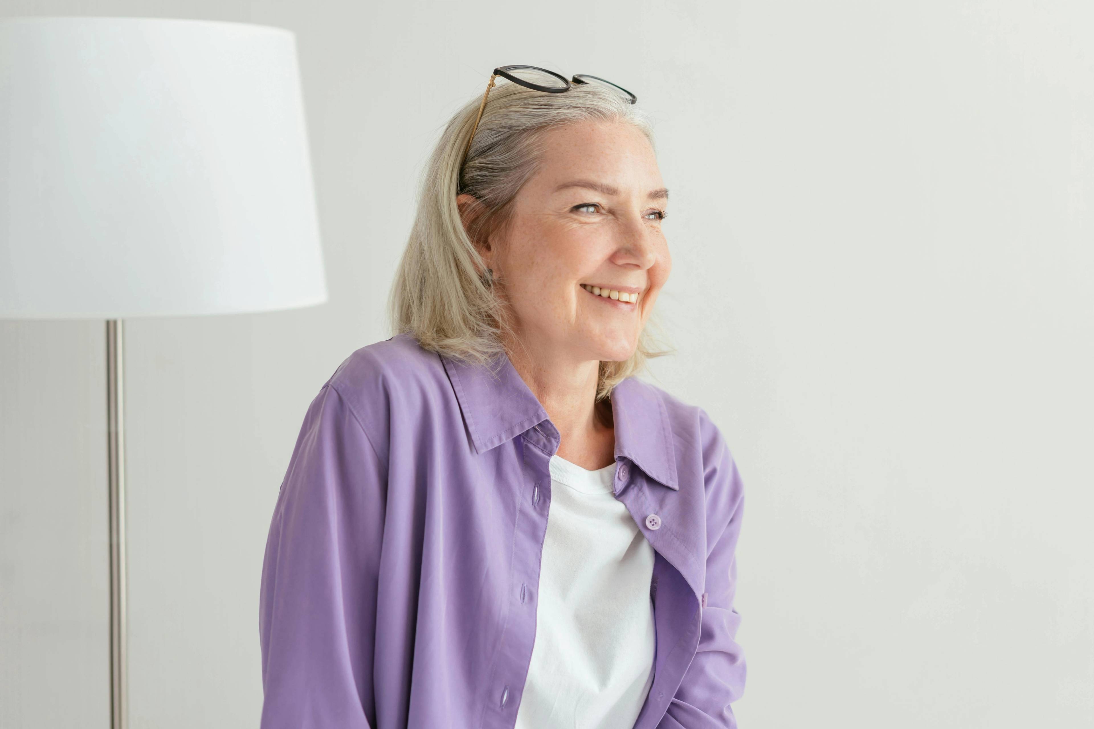 female in purple shirt wearing glasses on top of head and smiling confidently in light environment