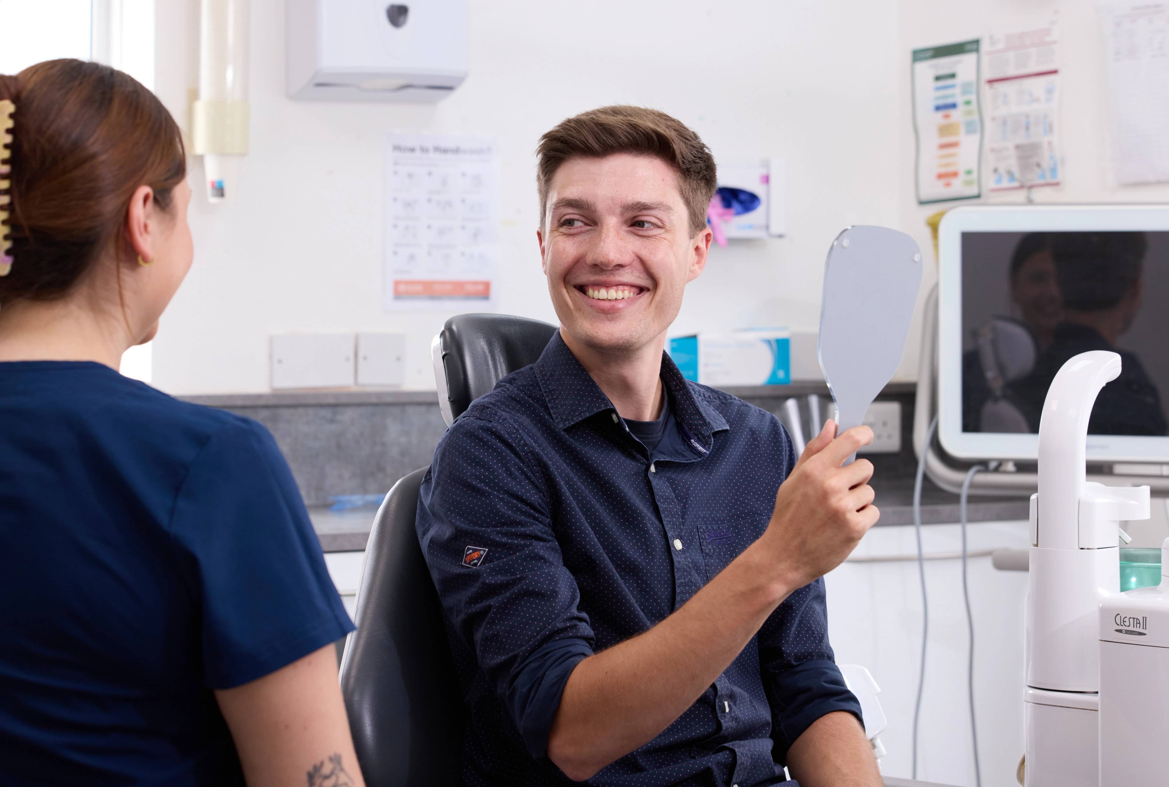 Young patient holding mirror and smiling at dentist after filling dental treatment